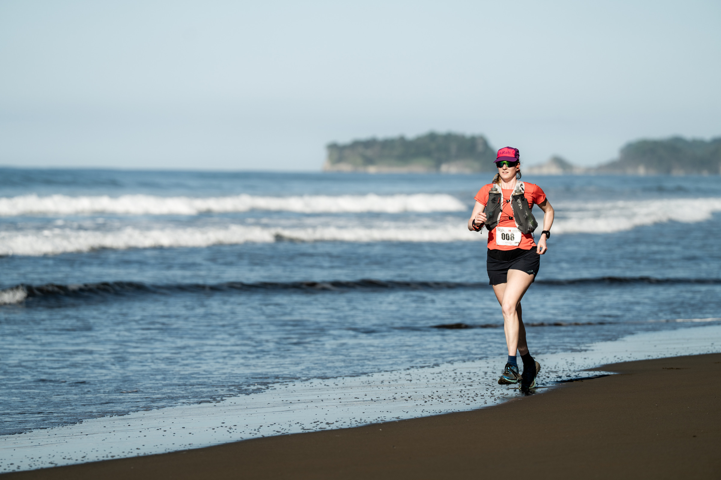 Løper på stranden i Costa Rica med bølger og en liten øy i bakgrunnen.