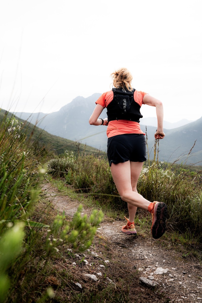 Løper sett bakfra, løper på en gresskledd fjellsti i Sør-Afrika.