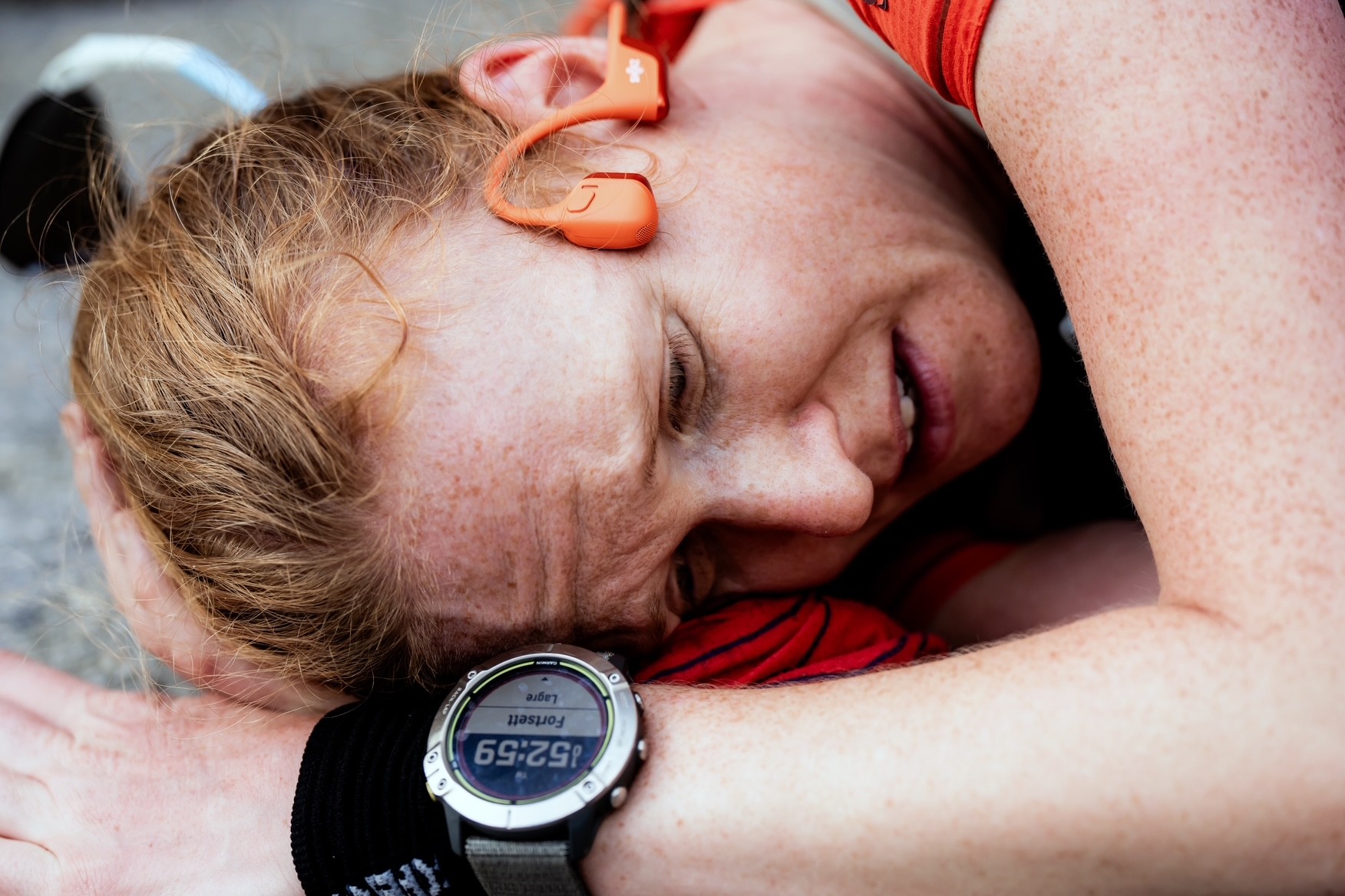 Portrett av løper som ligger på bakken og ser veldig sliten ut. Har på Garmin klokke og Shokz.